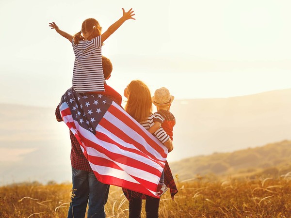 Family wrapped in an American flag overlooking golden hills at sunset, celebrating a patriotic holiday weekend at Gateway Canyons Resort in Wyoming